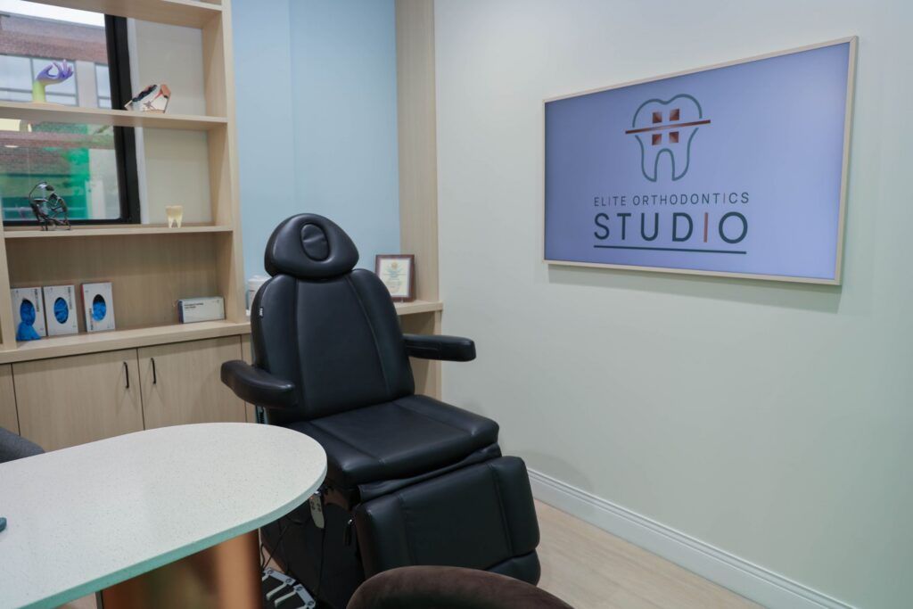 Elite Orthodontics Studio office treatment room with a chair and the practice logo on a wall screen